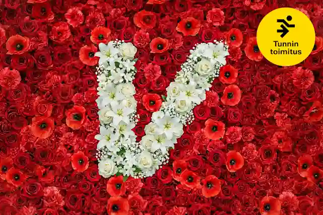 Punaisista kukista koostuva tausta, jonka keskellä valkoisista kukista muodostettu V‑kirjain. Oikeassa yläkulmassa keltainen merkki, jossa teksti ”Tunnin toimitus”.