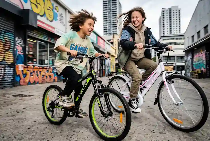 Kaksi lasta pyöräilee urbaanissa maisemassa Atalan ja Inseran uusilla pyöräillä. Tutustu! (Ai-työkalulla tehty kuva)