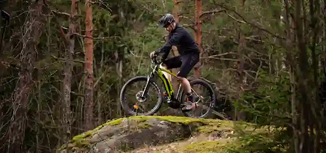 Pyöräilijä pyöräilee mäkeä alas metsässä.