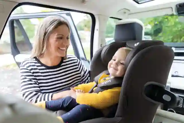 Äiti ja lapsi hymyilevät toisilleen autossa. Lapsi istuu turvaistuimessa ja äiti on ovensuulla.