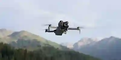 Drone lentää vuoristomaisemassa, taustalla epätarkkoja vuoria ja metsää.