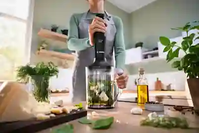 Tehosekoitin keittiössä basilikan, valkosipulin, oliiviöljyn ja parmesaani-juuston keskellä