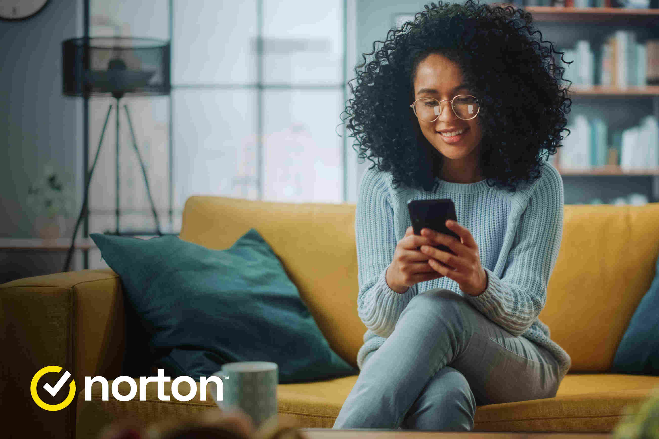 Henkilö katsoo puhelinta sohvalla istuen. Vasemmalla alanurkassa Norton-logo.
