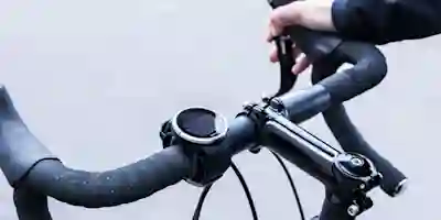 A hand grips a road bike handlebar with a cycling computer mounted on it.