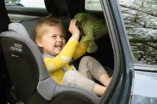 Lapsi istuu Britax Römerin turvaistuimessa autossa ja leikkii iloisena vihreällä pehmolelulla. Tutustu turvaistuimiin!