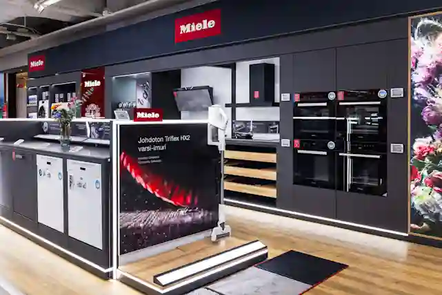 Interiör från Miele-butiken med diskmaskiner, ugnar och köksfläkt på display. I mitten en annons för den trådlösa Triflex HX2 handstickdammsugaren.