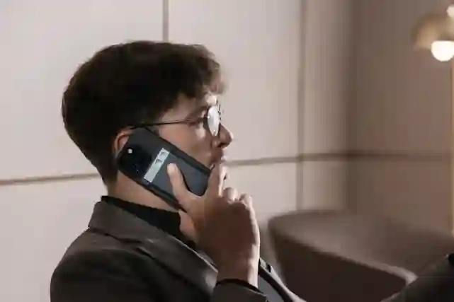 A person wearing glasses talks on the phone indoors.