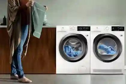 En person håller en grön handduk framför en Electrolux tvättmaskin och torktumlare med blå tvätt i.