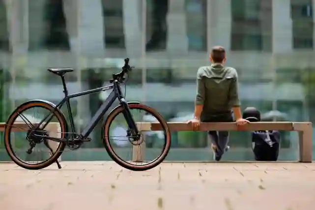 Pyöräilijä istuu penkillä vieressään kypärä ja reppu. Etualalla polkupyörä.