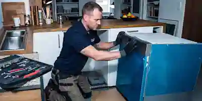 En installatör installerar en ny diskmaskin från Ström i köket, med verktygslådan bredvid.
