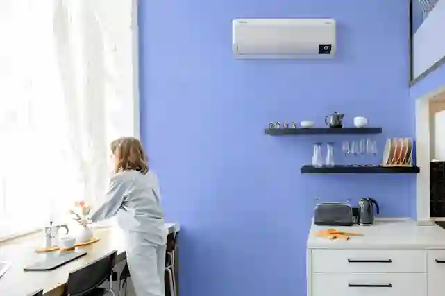 Nainen seisoo modernissa keittiössä jonka seinällä on ilmalämpöpumppu.
