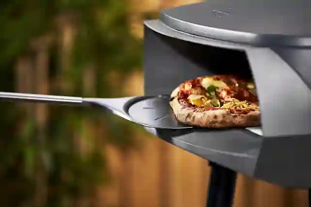 Ooni-pizzaugn utomhus, pizzaspade och en färsk pizza som gräddas i ugnen.