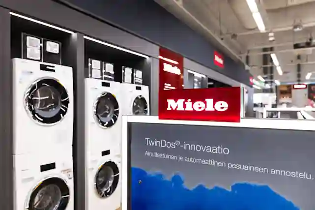 Miele-pesukoneiden myymälänäyttely, etualalla TwinDos-innovaatiota esittelevä kyltti ja punaisella Miele-logo.