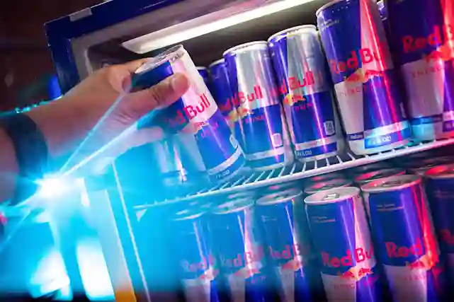 A person taking a Red Bull from a cooler.