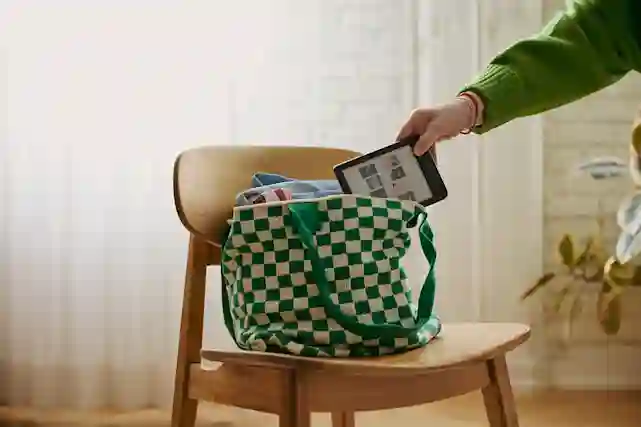 Kobo Clara -lukulaitteen näytöllä monta kirjan kantta. Itse lukulaite on pakattu mukaan otettavaan laukkuun.
