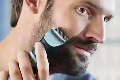 A man trims his beard with an electric beard trimmer.