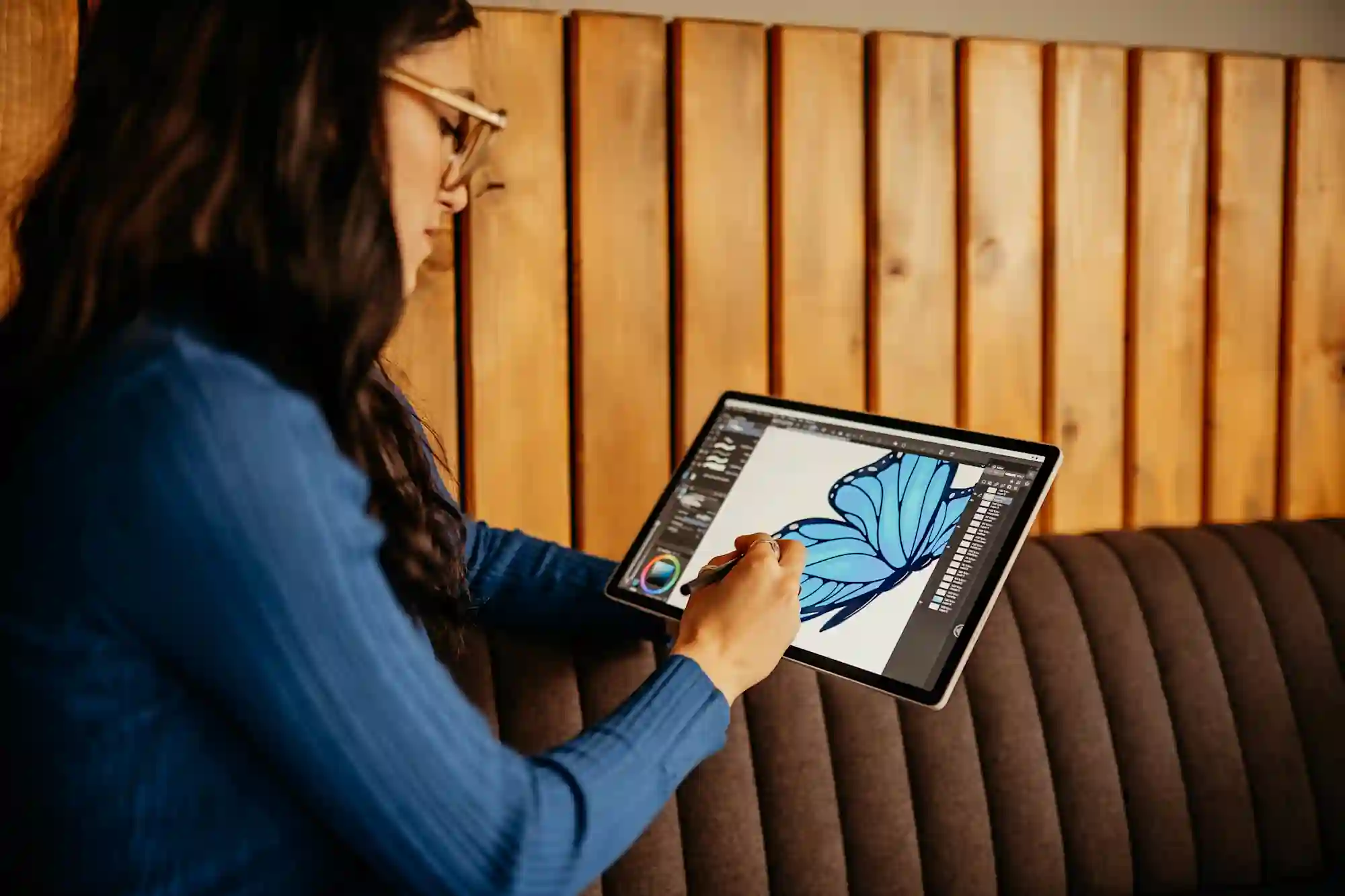 A woman draws blue flower graphics with a digital pen on a Wacom tablet in a graphics program.