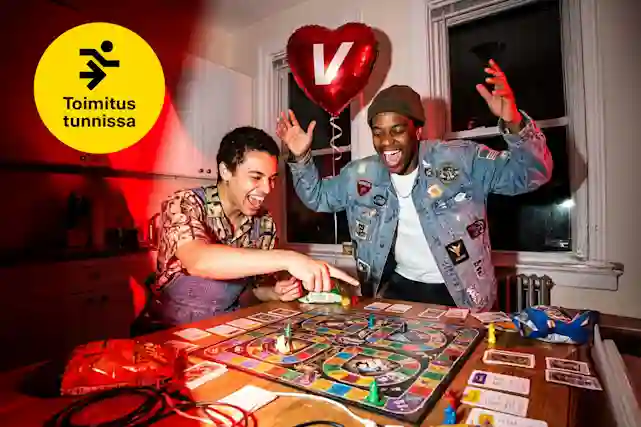 Kaksi ystävystä pelaa keittiössä lautapeliä ja nauravat hervottomasti. Taustalla sydämenmuotoinen V-logo ilmapallo. Vieressä myös pallura, jossa teksti:"Toimitus tunnissa".