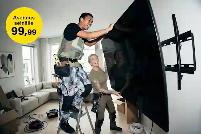 Kaksi asentajaa asentaa iloisesti nauresekellen isoa televisiota seinälle. Verkkokauppa.comista television asennus seinälle 99,99 € tv:n oston yhteydessä.