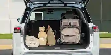 Open trunk of a white car filled with luggage: a stroller, teddy bear, blankets, and bags.