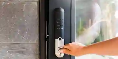 A hand opens a black glass door with a smart lock featuring a numeric keypad and a silver handle.