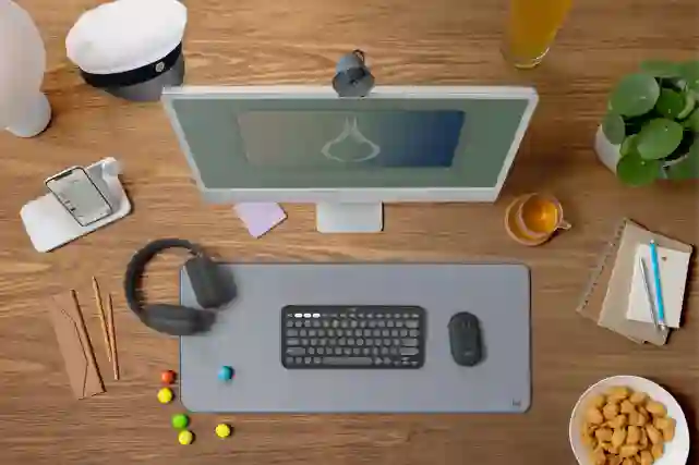Työpöydälle tietokoneen näyttö, näppäimistö, kuulokkeet, muistiinpanovehkeet, lamppu ja Ylioppilaslakki.