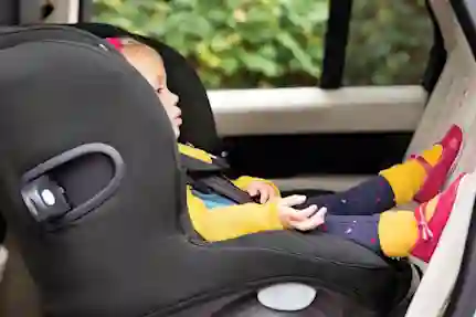 A child sleeps in a black car seat, wearing a yellow shirt and pink shoes.