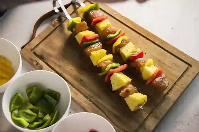 Grillade spett med kyckling, ananas och färgglada paprikor på en träskärbräda.