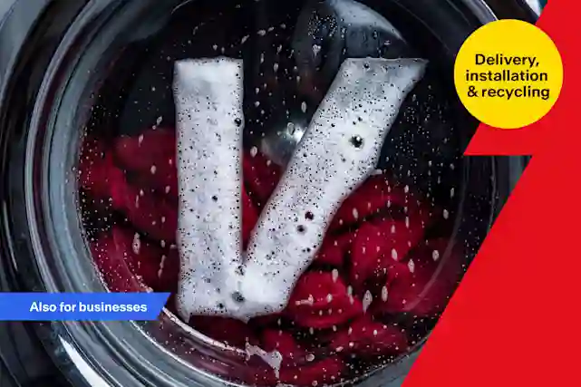 Top-down view of the inside of a washing machine drum, with foamy detergent forming a V-shape against red clothes.