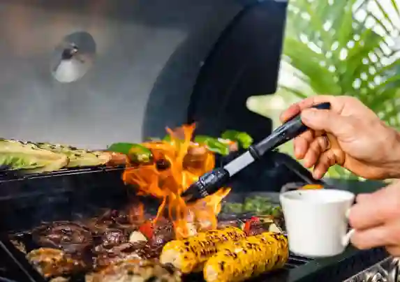 Lähikuvassa liekit nousee ylös, kun kokki voitelee grillissä olevia ruokia.