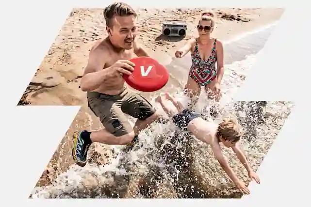 Perhe leikkii rannalla V-logolla varustetun punaisen frisbeekiekkon kanssa, taustalla boombox hiekalla.