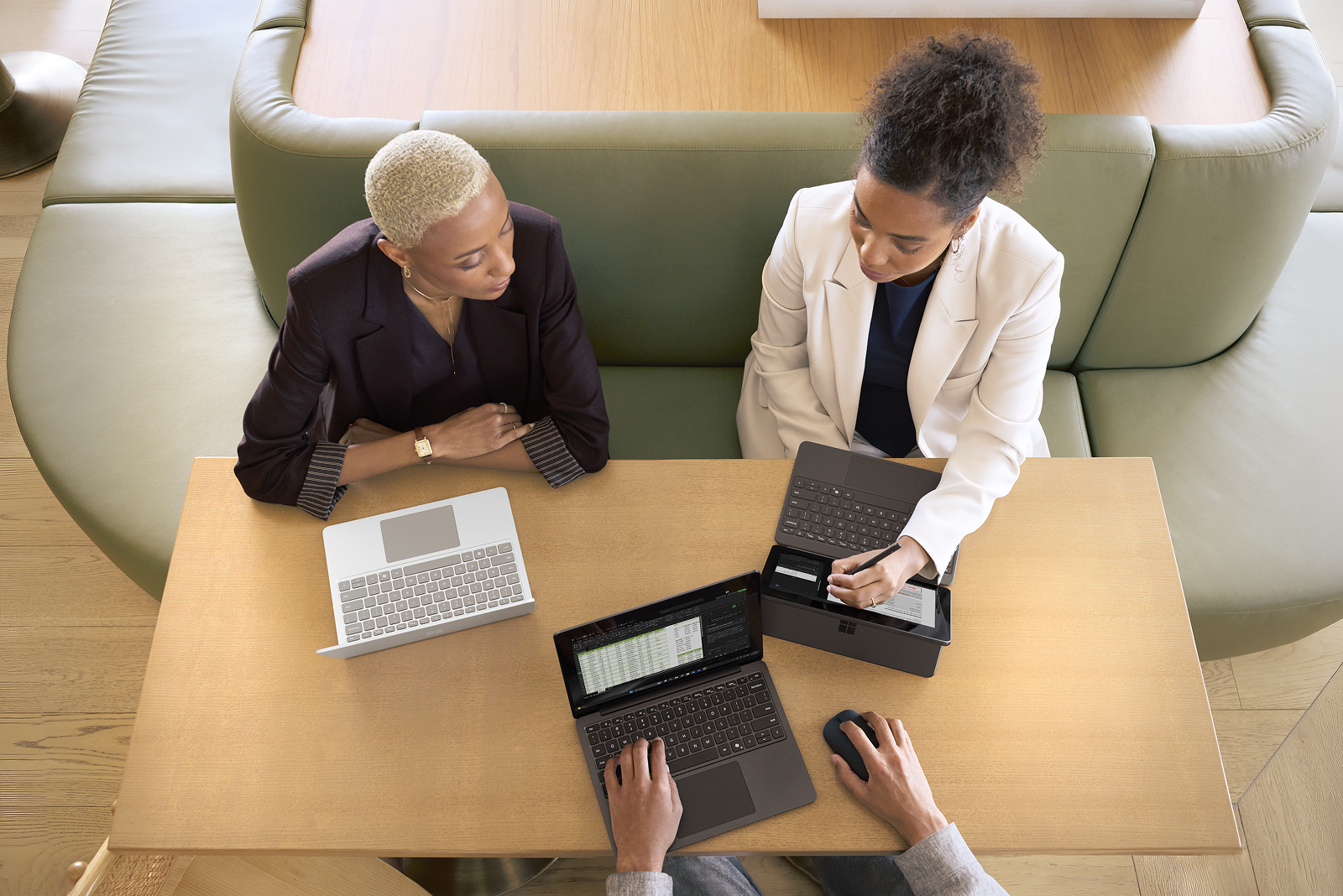 An top-down view of three coworkers collaborating on three different Surface devices while sitting at a table