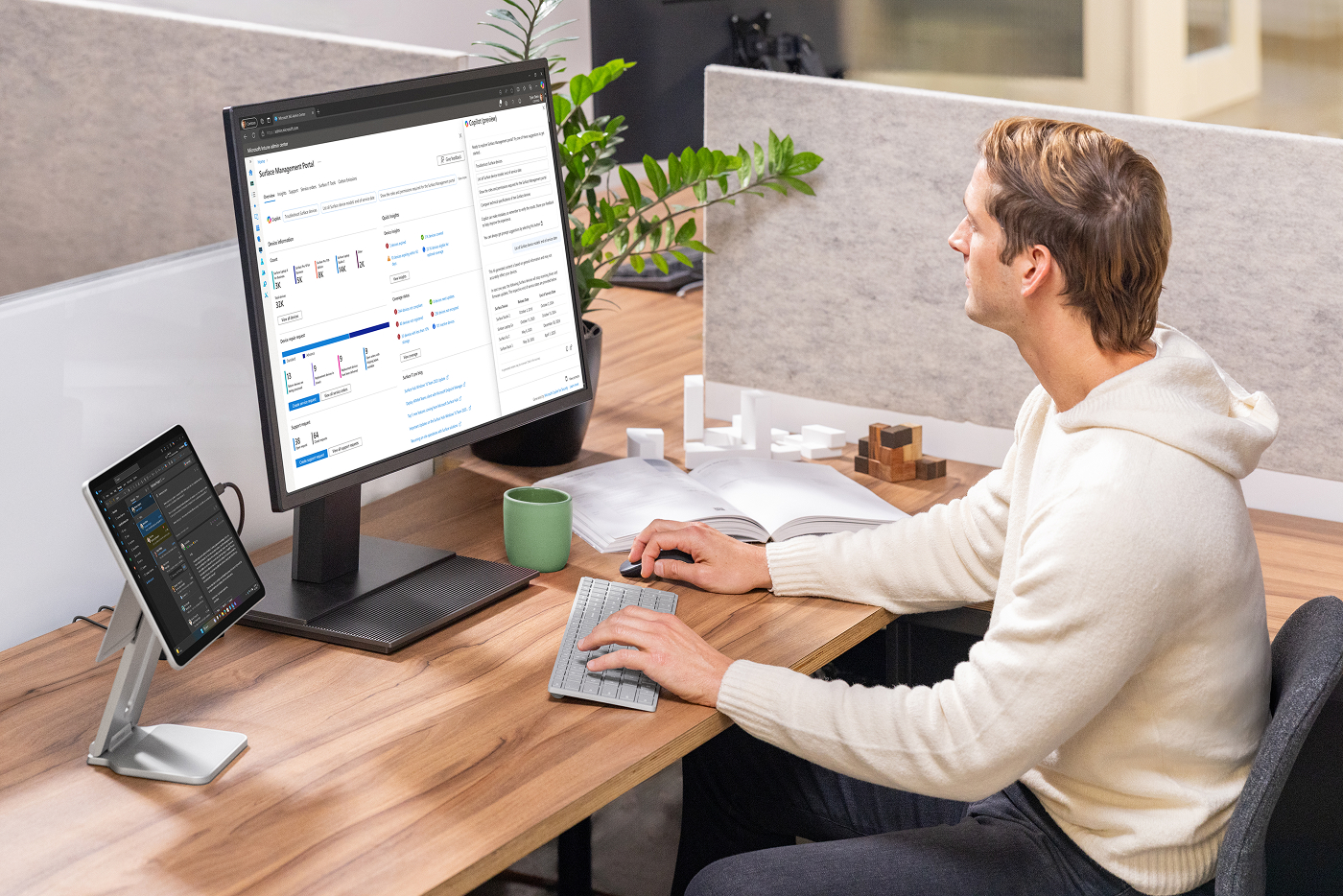 A man works on a monitor at an office desk using a Surface keyboard, mouse, and Pro 2-in-1.