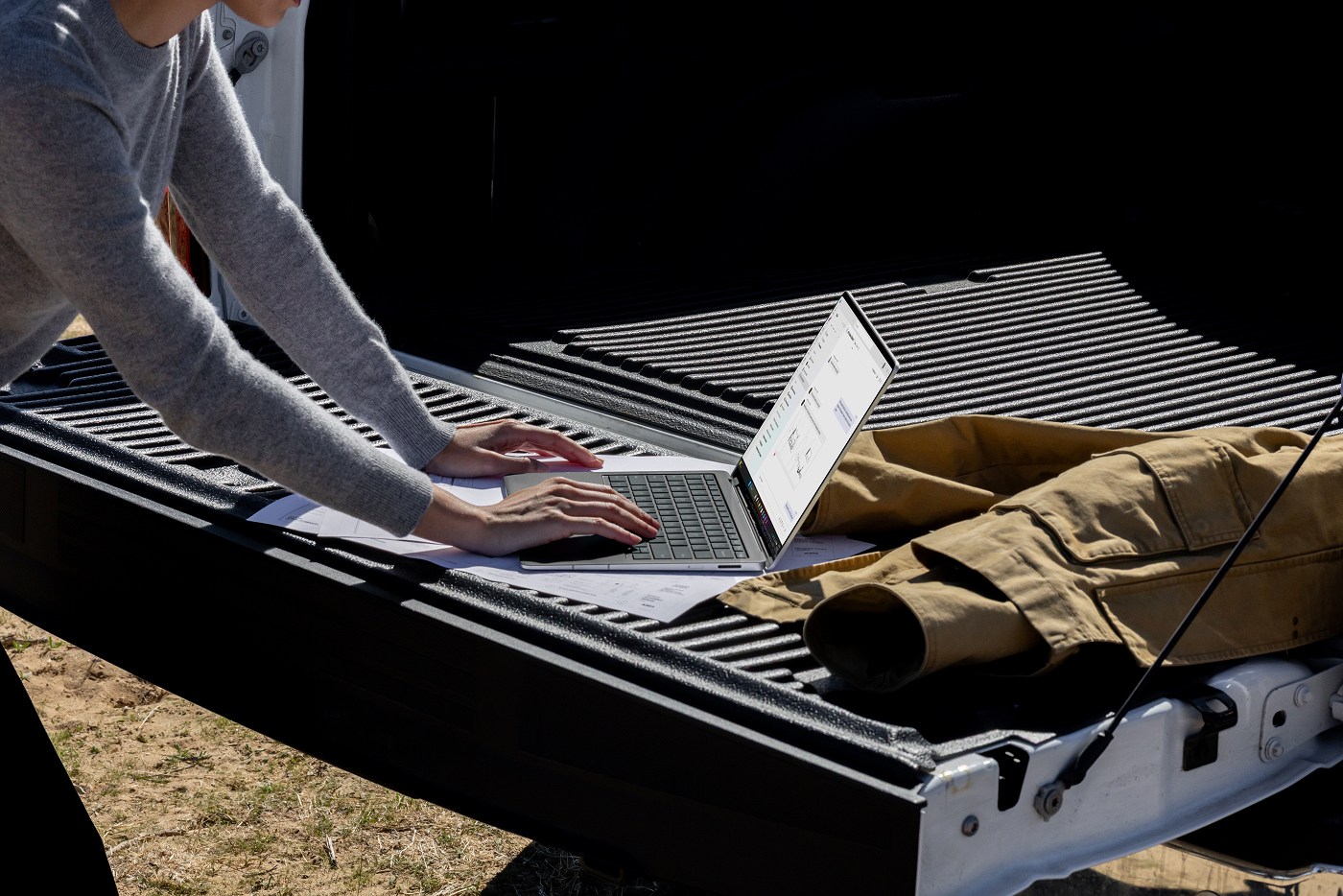 A woman working on a Surface Laptop outside on the bed of a truck