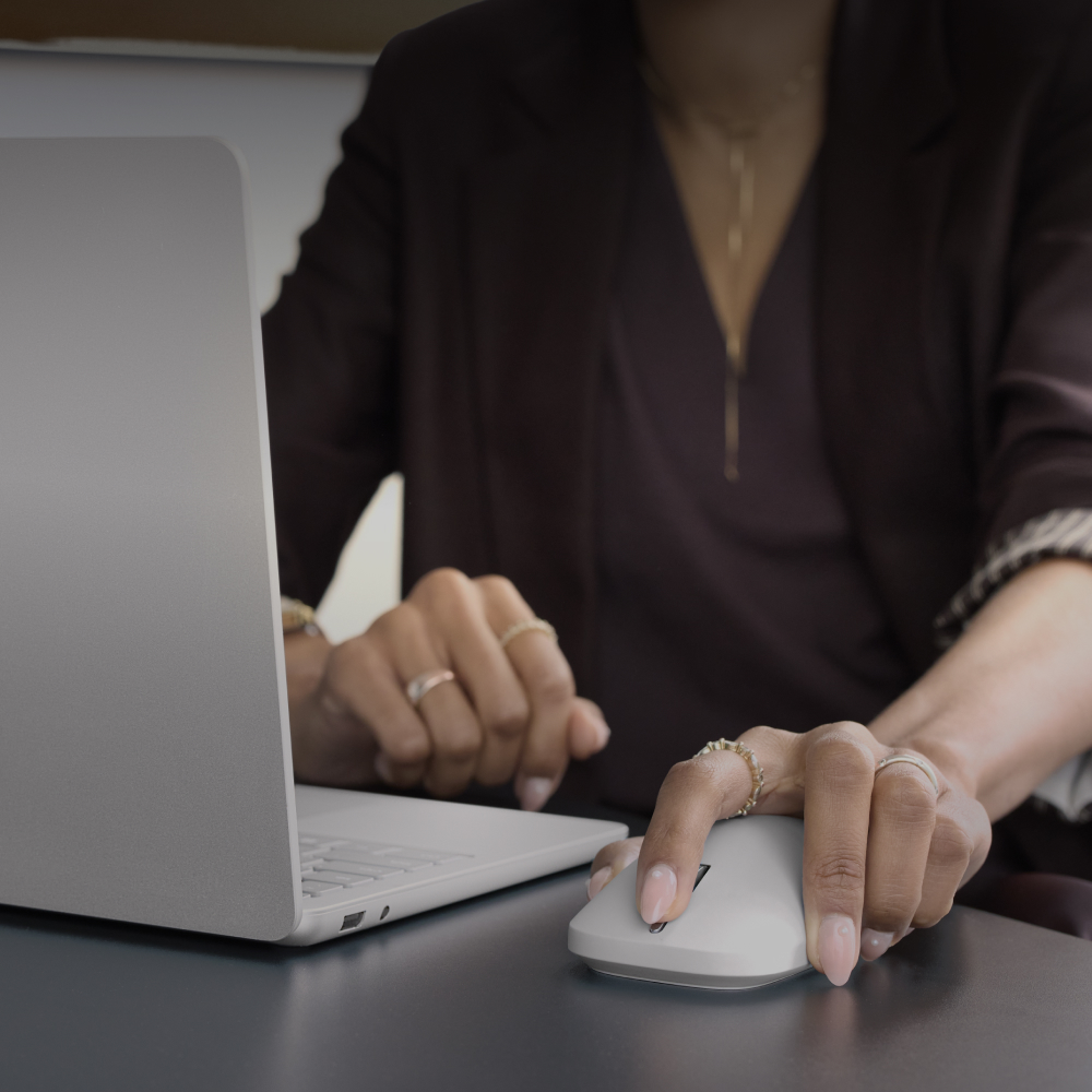 A woman working on a Surface Laptop while scrolling with the new Surface Mouse at a desk