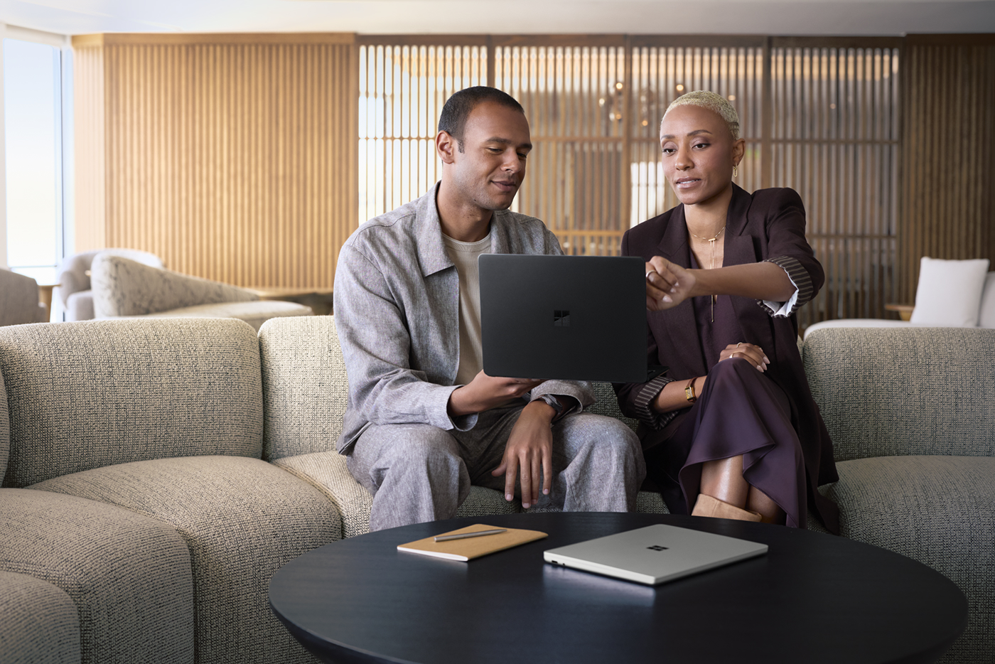 A man and woman sitting on a couch working on a Surface Laptop