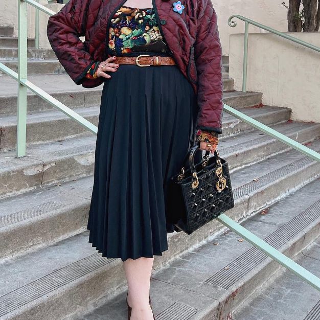 a woman in a long black skirt and burgundy jacket holding a black Christian Dior Lady Dior