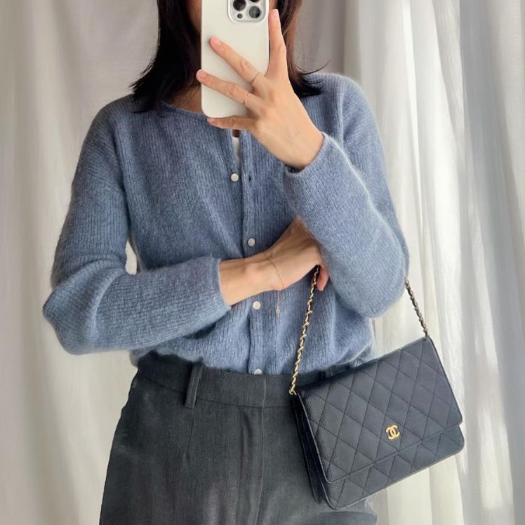 a woman in a grey sweater Holding a black Chanel WOC Wallet on Chain