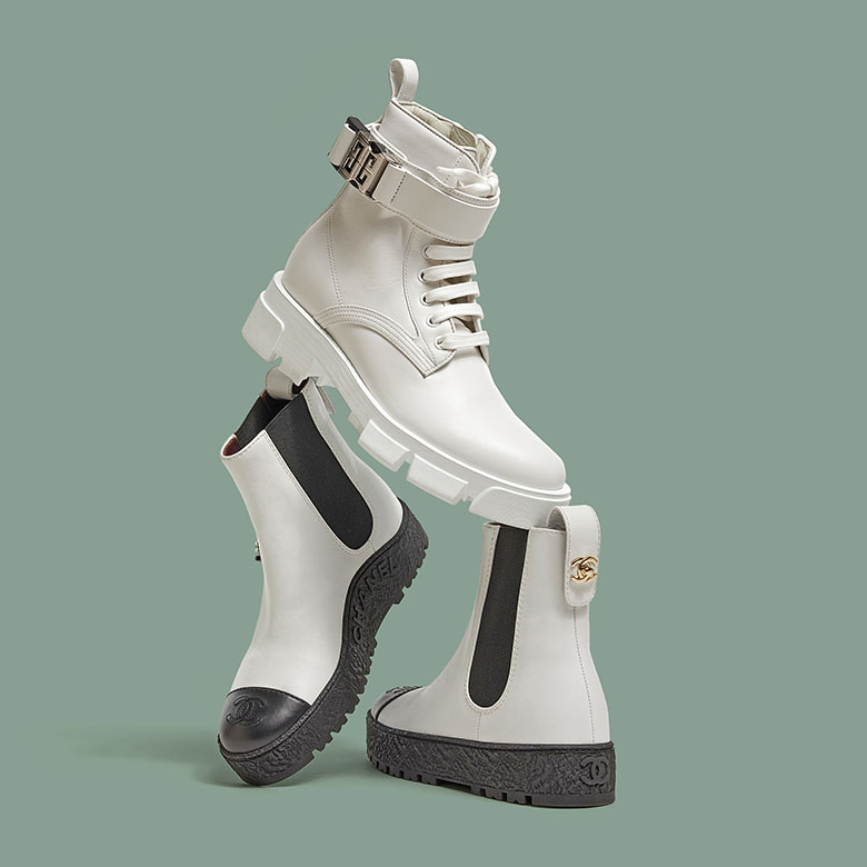 one white Givenchy Terra boot balancing on a pair of white Chanel cap toe ankle boots
