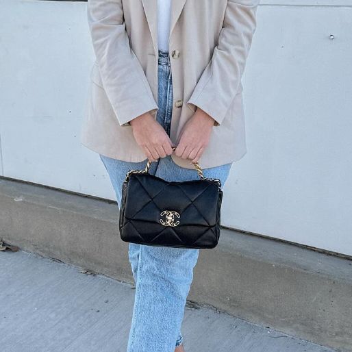 woman in beige blazer and denim pants holding a black Chanel 19