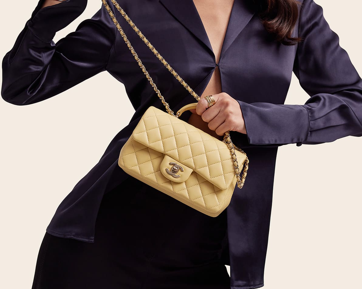 a woman in a dark blue satin shirt and matching pants holding a light yellow Chanel rectangular mini flap bag with top handle