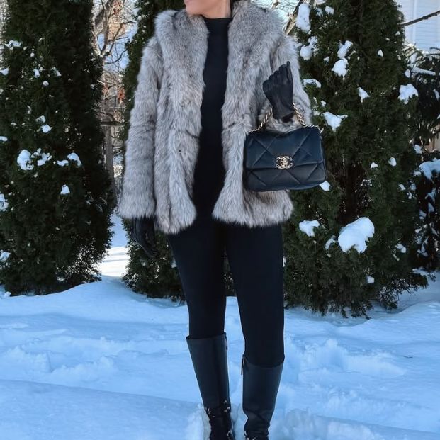 a woman in black pants and a grey fur coat holding a black Chanel 19 bag