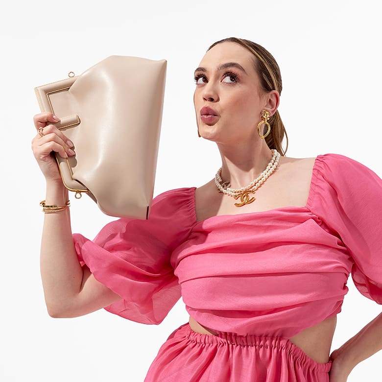 woman in pink dress holding a beige Fendi First bag up to her face
