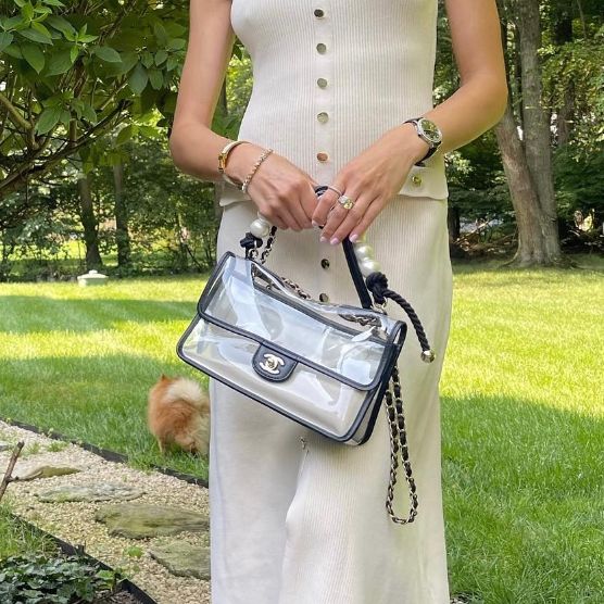 a woman in a cream matching sleeveless top and skirt holding a CHANEL Lambskin PVC Sand By The Sea Flap With Pearl Strap Black