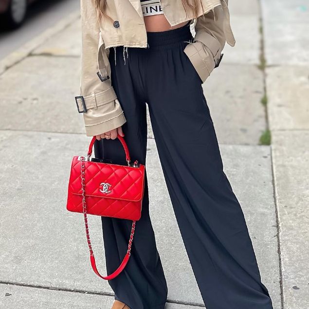 Woman in beige cropped trench coat and navy blue wide leg pants holding a red Chanel Trendy Bag