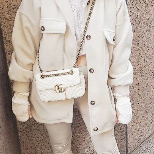 A woman in a white coat wearing a white Gucci Marmont crossbody bag