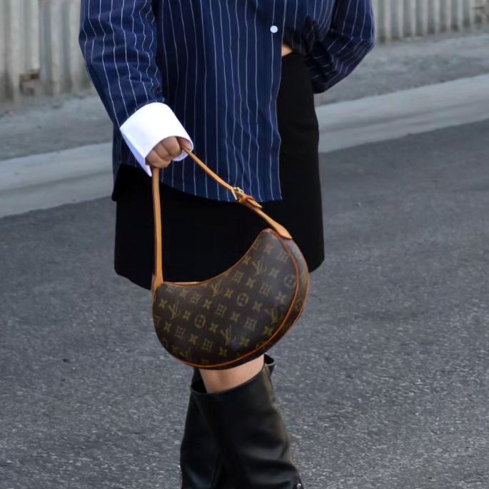 Woman in navy pinstripe top and black skirt holding a Louis Vuitton Monogram Croissant bag