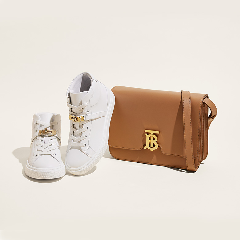 one pair of white Hermes high top Day sneakers next to one brown Burberry TB bag