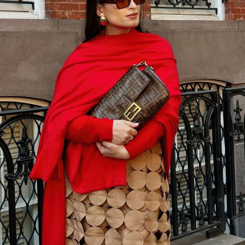 a woman in a red long sleeve wrap top and beige skirt holding a Fendi Baguette