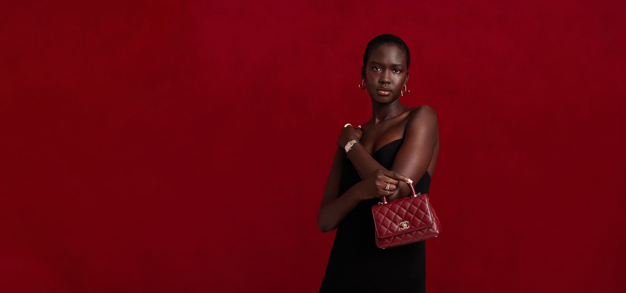 a woman in a black strapless dress in front of a red velvet background holding a red Chanel mini coco handle